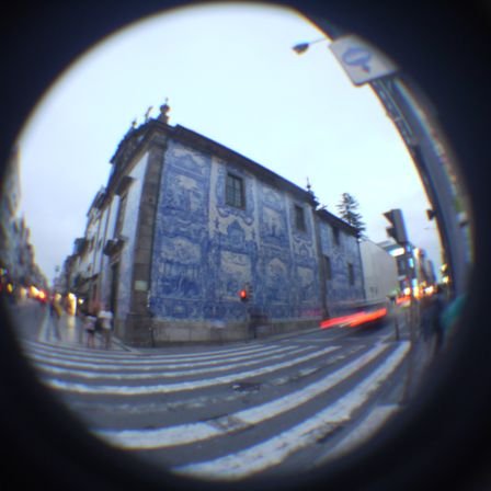 Foto de uma igreja em uma esquina. Ela tem toda a parede decorada com azulejos formando um desenho bem detalhado em azul, mas dificil de entender na foto. Na frente tem riscos da luz de freio de um carro que passou na mesma hora.