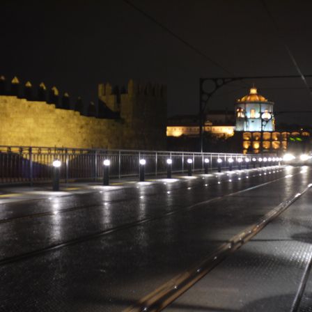 Foto de uma ponte, ela é de metal e segue pra direita, vários pequenos postes de luz da altura de uma pessoa adulta.