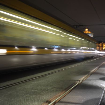 Foto de uma ponte, ela é de metal e segue pra direita, da pra ver o vulto de um metrô passando.