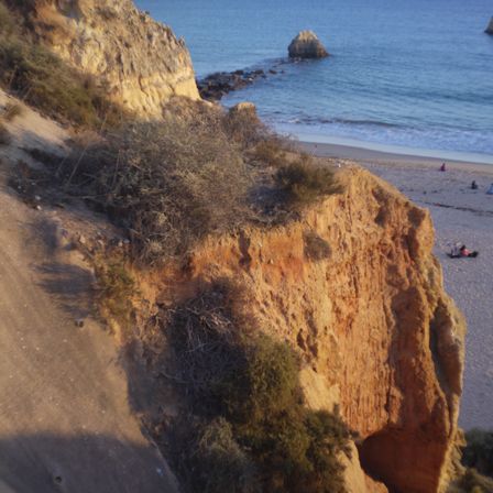 Uma formação rochosa cobre toda imagem a esquerda, a direita da pra ver o mar e uma parte da areia da praia.