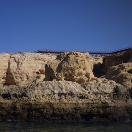 Foto de uma formação rochosa a beira do mar. É possível ver vários "furos" e cavernas nela