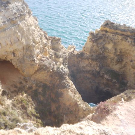 Foto de outra formação rochosa, são duas uma bem da esquerda da imagem e outra a o fundo vem do lado direito. Atrás da pra ver o mar.